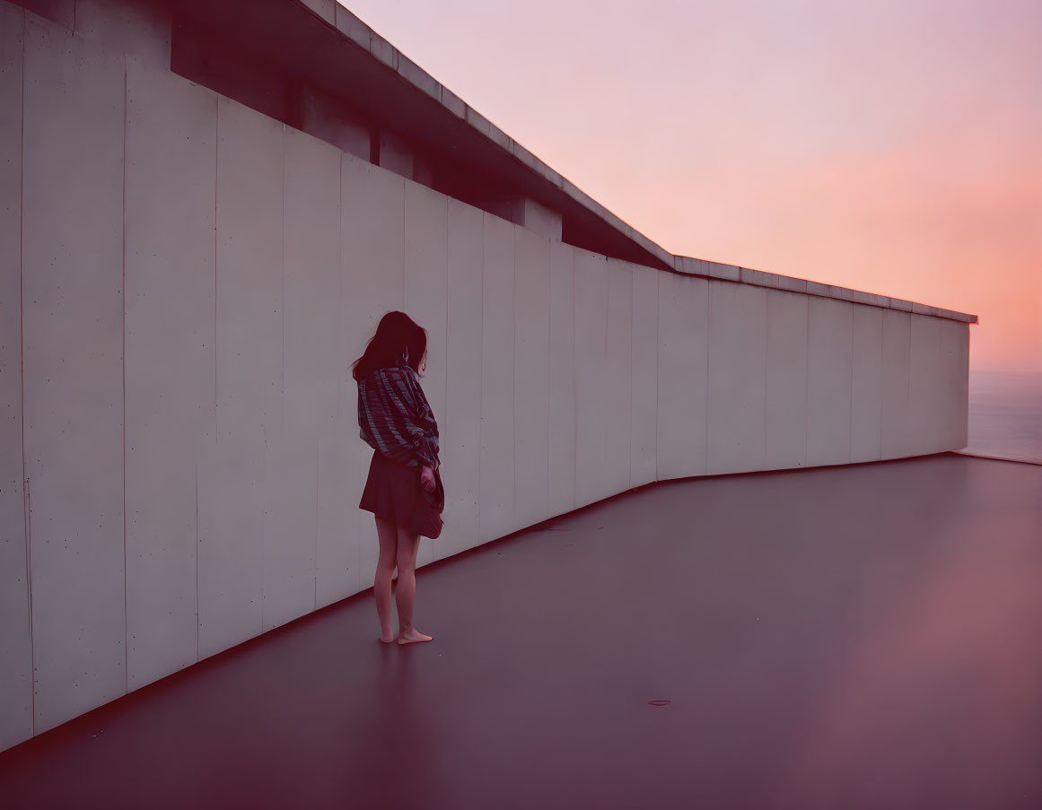 Person standing by concrete wall at pink sunset