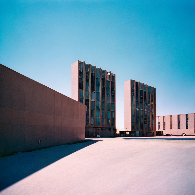 Modern architectural buildings under clear blue sky with high wall and empty concrete ground