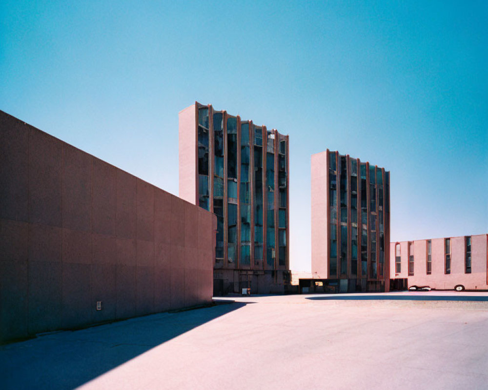 Modern architectural buildings under clear blue sky with high wall and empty concrete ground