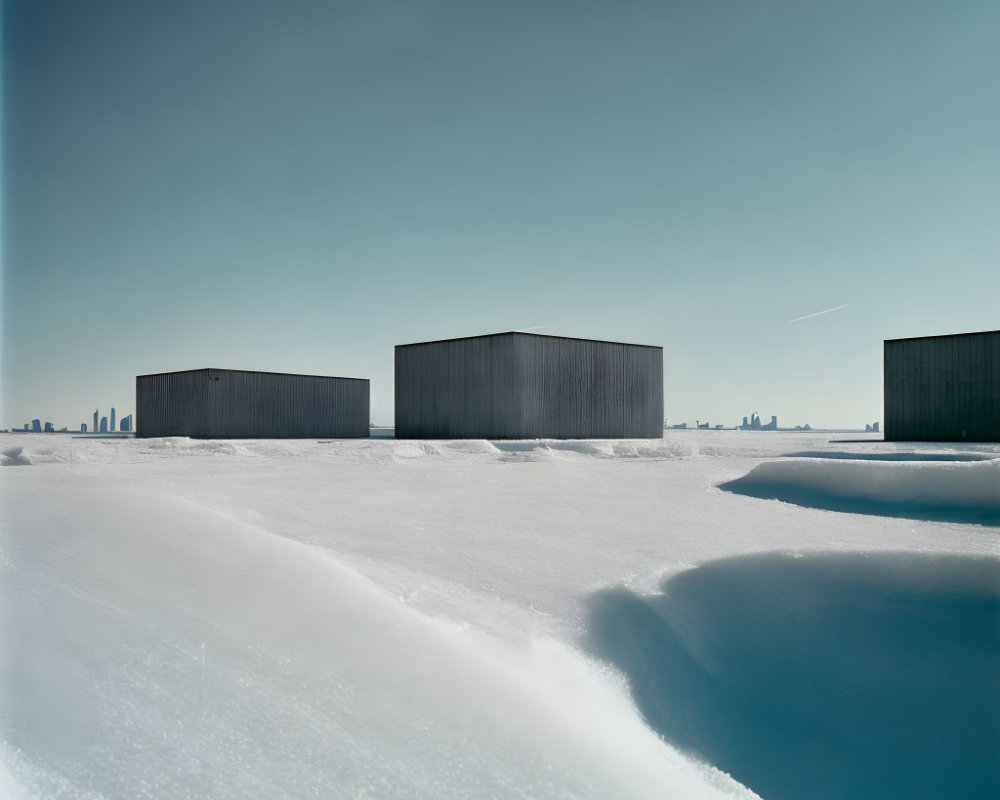 Dark rectangular buildings in snowy landscape with city skyline under clear blue sky