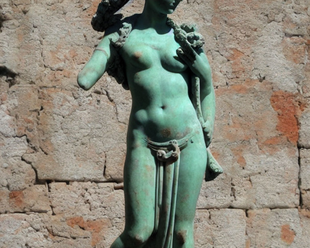 Classical bronze statue of female figure against textured stone wall