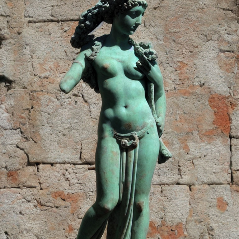 Classical bronze statue of female figure against textured stone wall