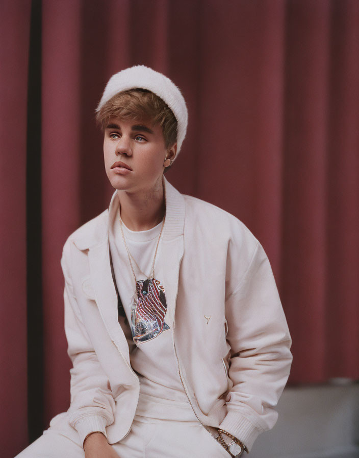 Styled Hair Person in White Outfit and Hat Against Maroon Background