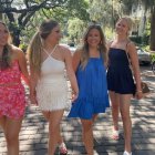 Four animated women in stylish dresses walking under tree-lined city street