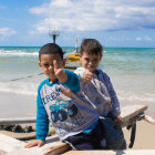 Children with striking eyes on beach with sailboat and dramatic sky.