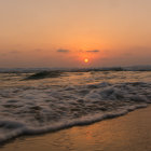 Vibrant orange sunset over turquoise beach waves and rocky outcrops