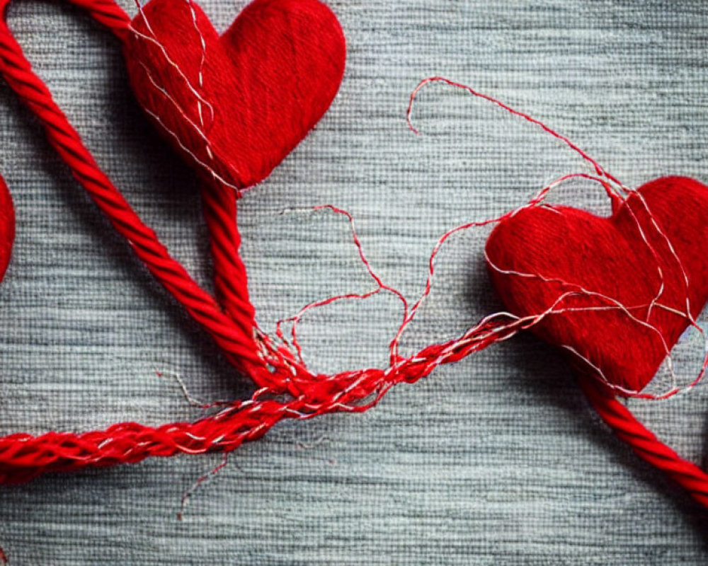 Red Fabric Hearts Connected by Thread on Gray Textured Background