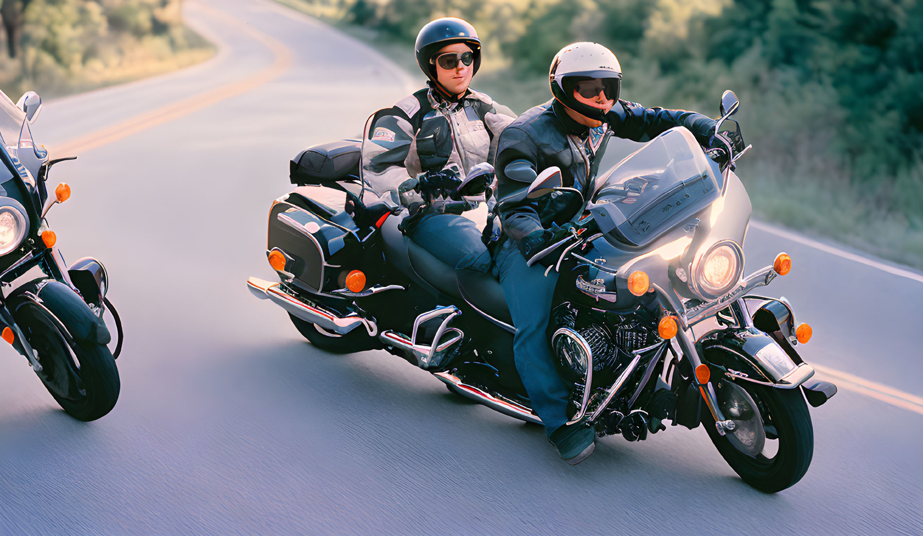 Two motorcyclists on curvy road with helmets and sunglasses, one on touring bike
