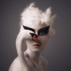 Monochromatic image of person with striking eyes holding feathered mask