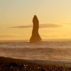 Isolated lighthouse on craggy islet at sunset with vintage planes