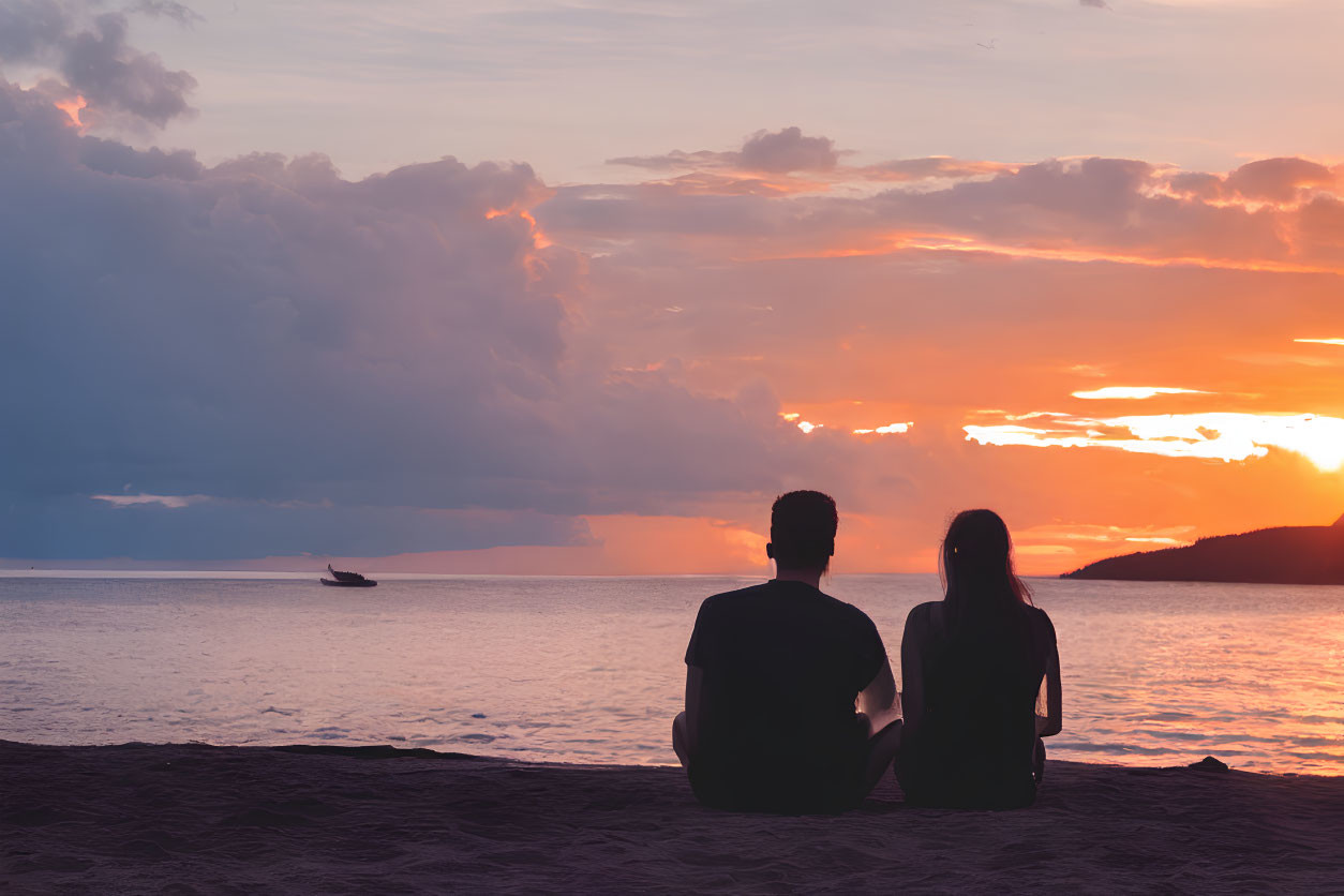 Beach sunset scene with two people and boat silhouette