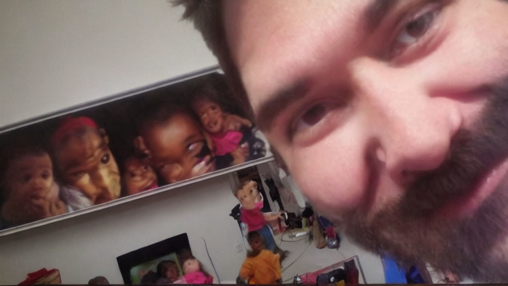 Man taking selfie with blurred background of children's toys and framed photo