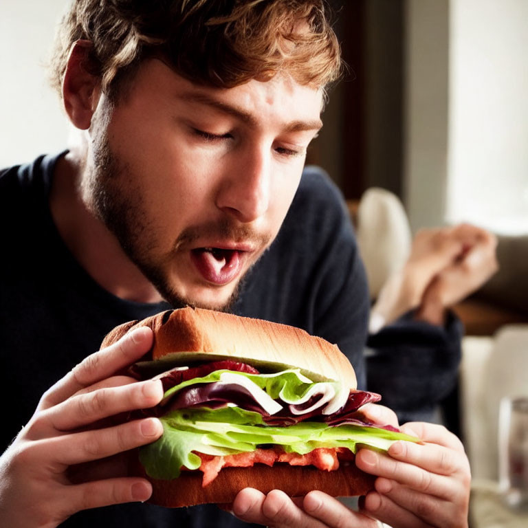 Bearded man eating a sandwich with lettuce, tomato, and meat