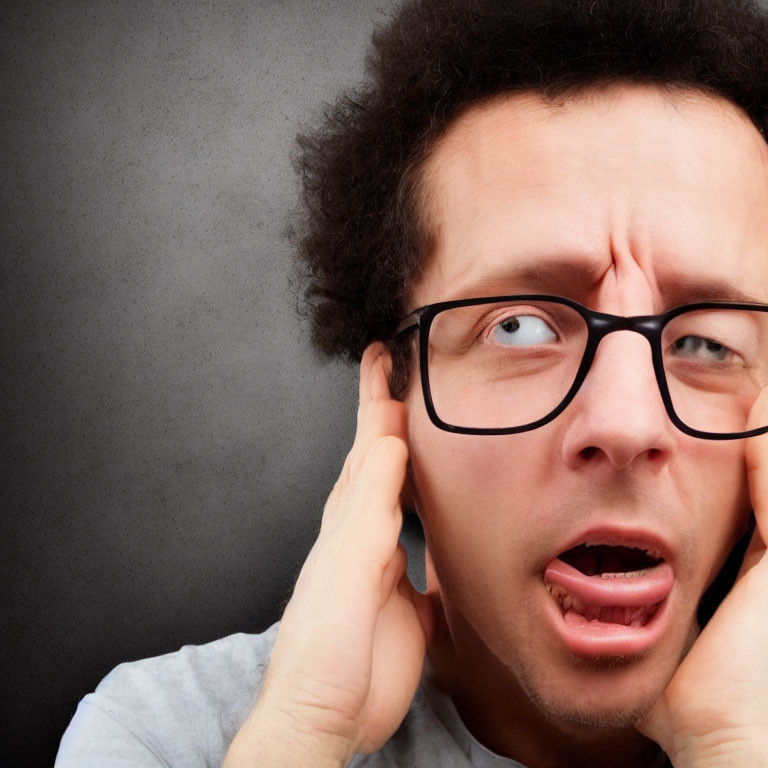 Curly-Haired Man in Glasses Expressing Frustration on Grey Background