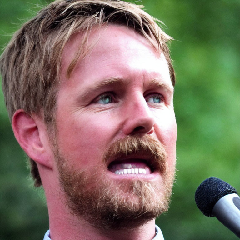 Bearded man speaking into microphone with intent gaze