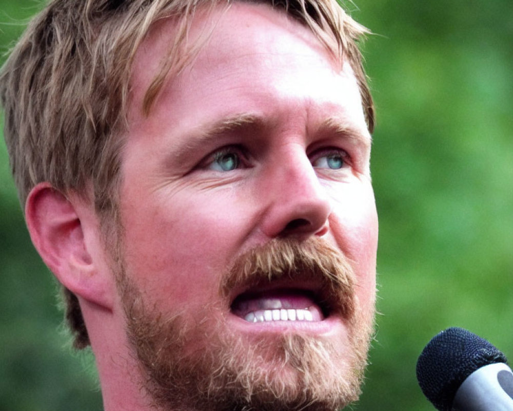 Bearded man speaking into microphone with intent gaze