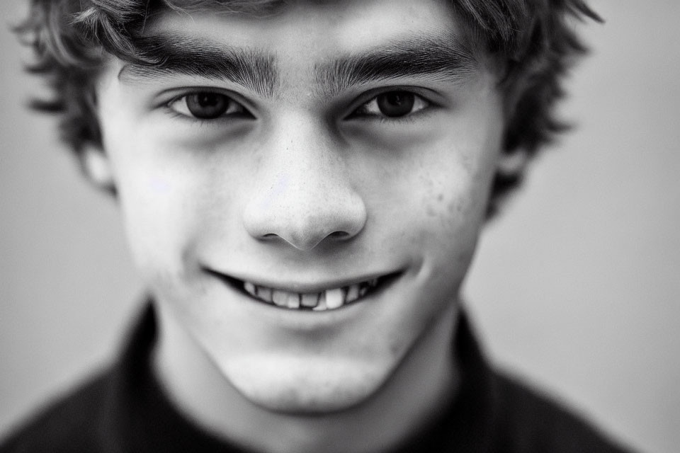 Monochrome close-up of smiling young male with curly hair and freckles