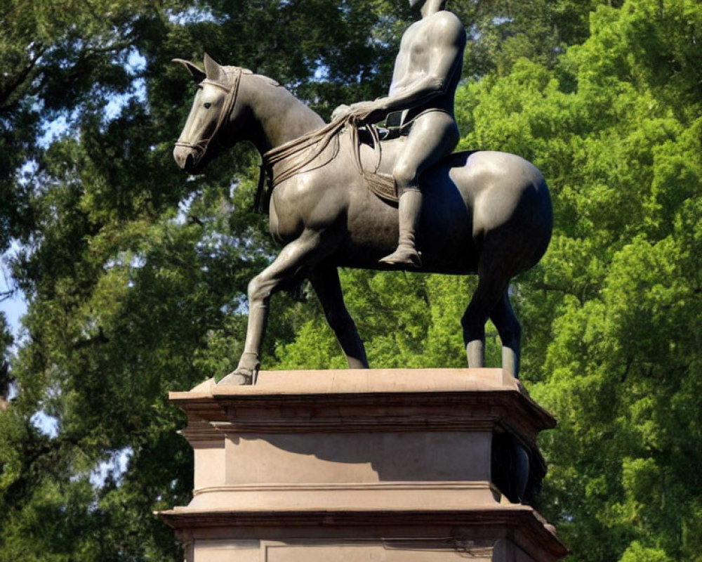 Bare-chested male rider statue on horse with trees in background