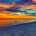 Colorful sunrise scene at calm beach with person in water and old pier under cloudy sky