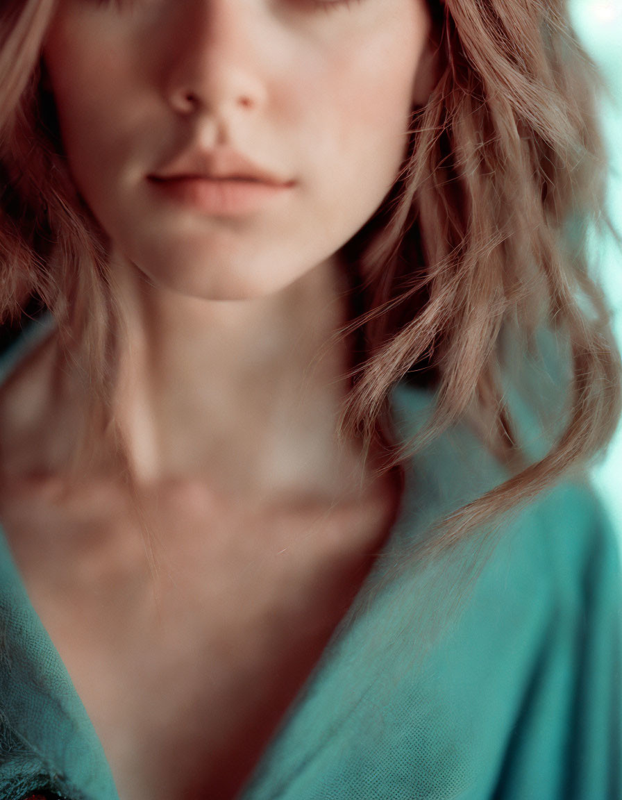 Woman with wavy hair in turquoise garment, serene expression, close-up shot.