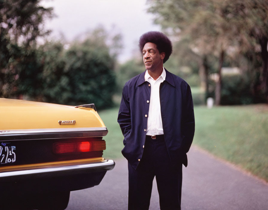 Man with Afro by Vintage Yellow Car in Greenery