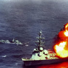 Battleship at sea fires front cannon, creating fireball & smoke