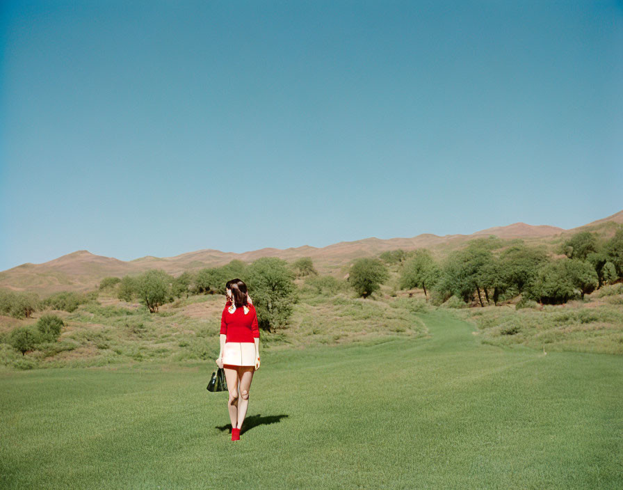 Person in Red Top Walking Across Green Field with Rolling Hills