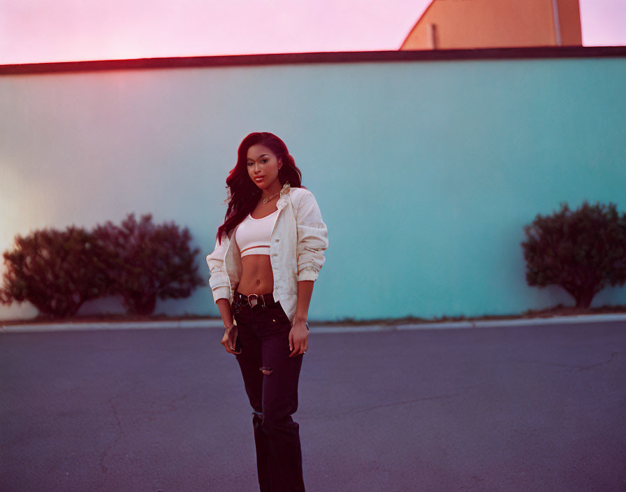 Woman in black pants and crop top poses against wall at sunset