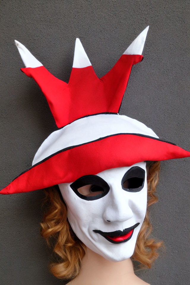 Red and white jester hat on person with white mask