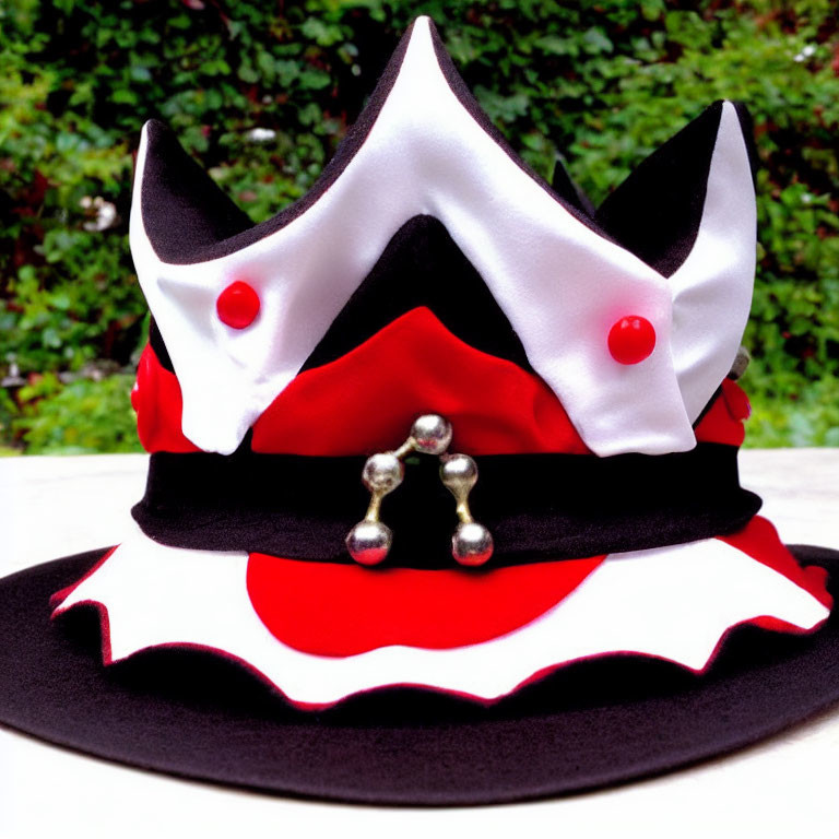 Colorful jester hat with black and white peaks, red pom-poms, silver bells, on