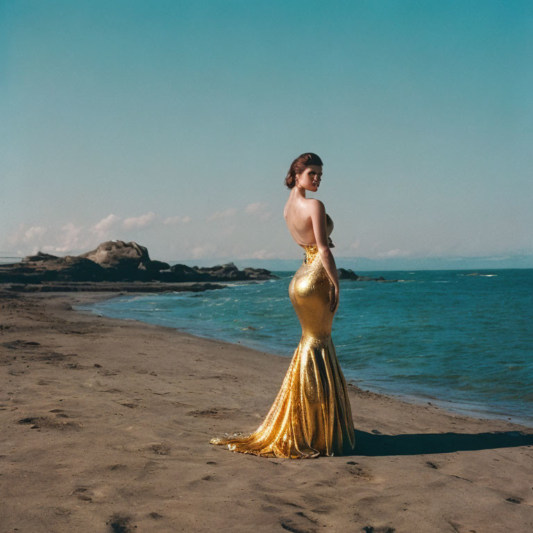 Woman in gold mermaid gown gazes at rugged beachscape