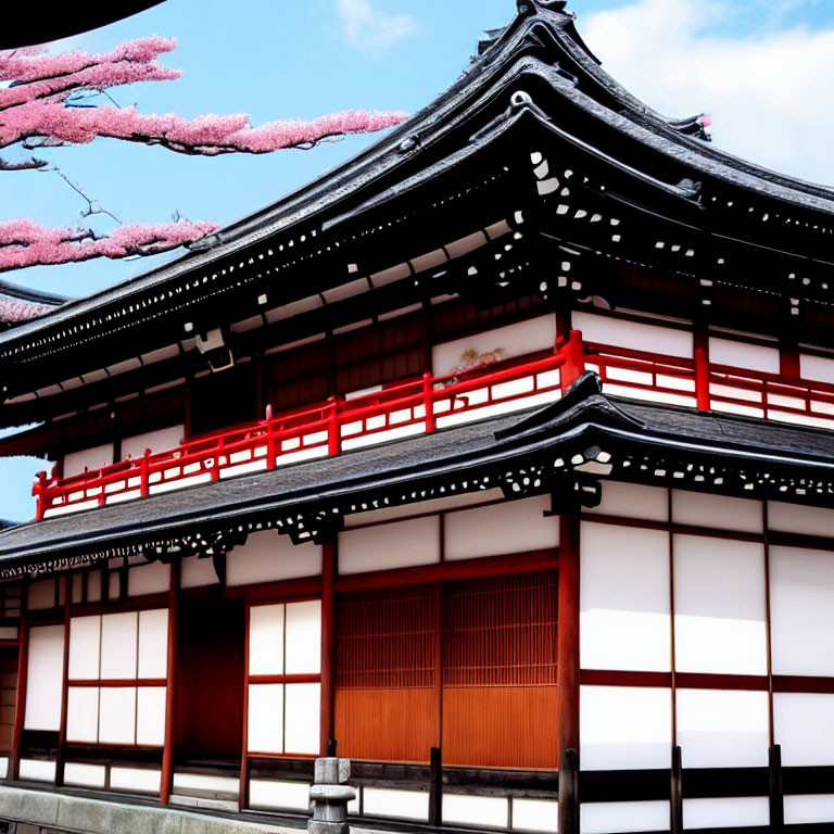 Traditional Japanese building with curved black tiled roof and cherry blossoms.