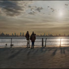 Silhouetted figures by railing admire city skyline at sunset