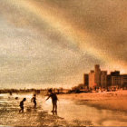 Colorful beach scene with multiple Ferris wheels and rainbow sky