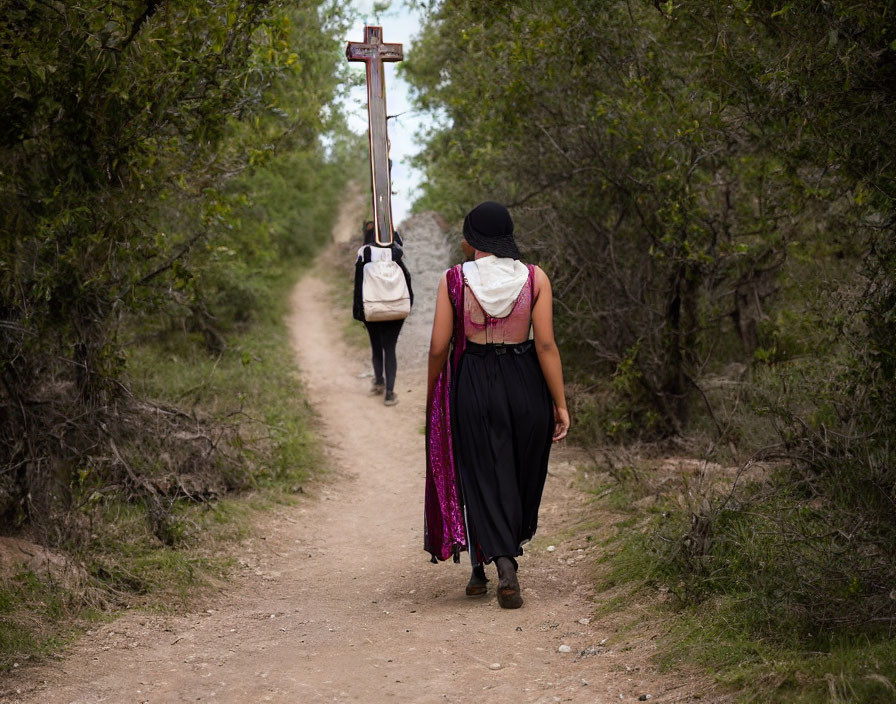 Two individuals walking with cross and backpack in green landscape