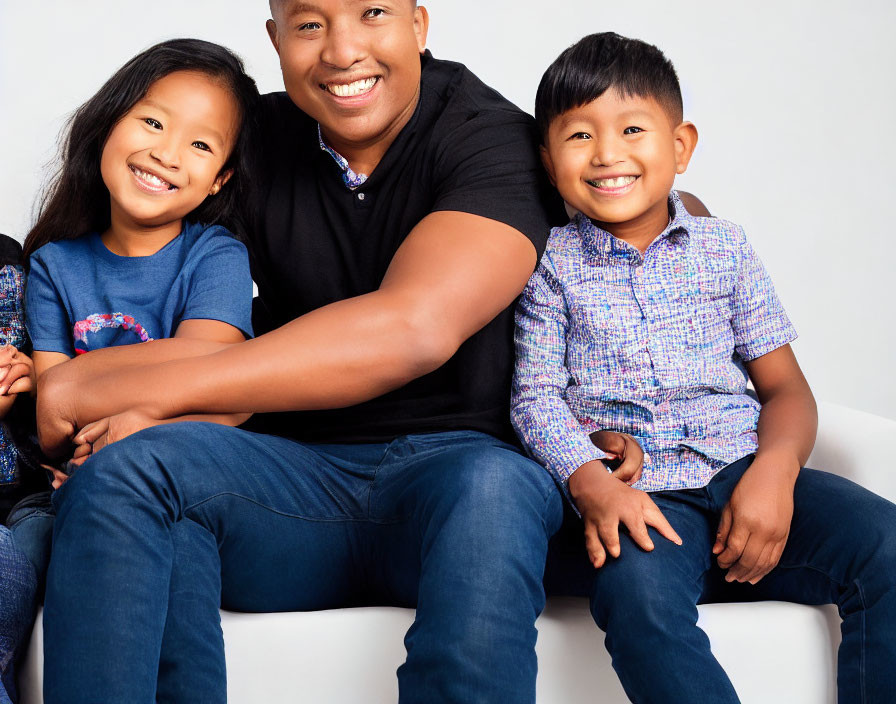 Smiling man in black polo shirt with happy kids on white sofa