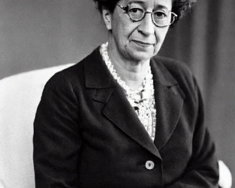 Monochrome image of seated woman in blazer and glasses