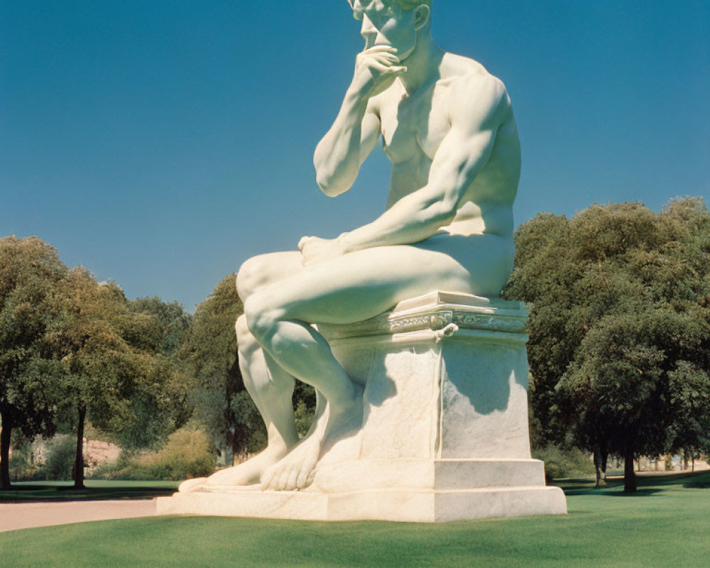 White Statue of Contemplative Man Amid Green Trees and Blue Sky