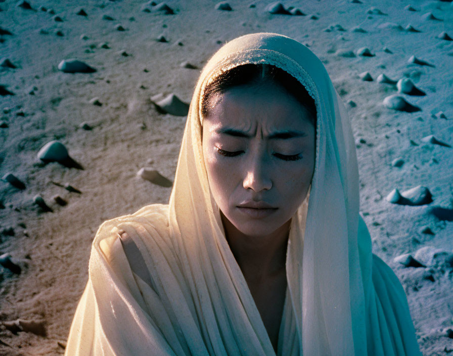 Contemplative woman in white shawl on sandy background