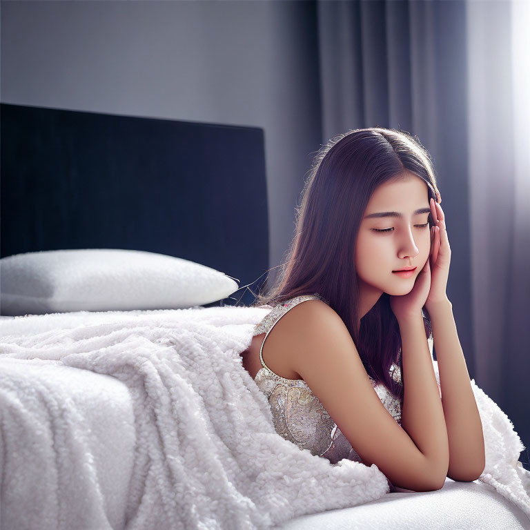 Young woman sitting beside a white bed in dimly lit room