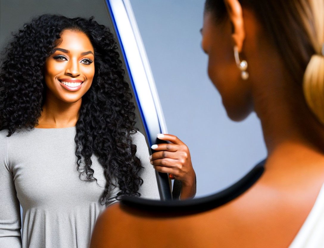 Curly-Haired Woman Smiling at Reflection in Mirror in Gray Dress