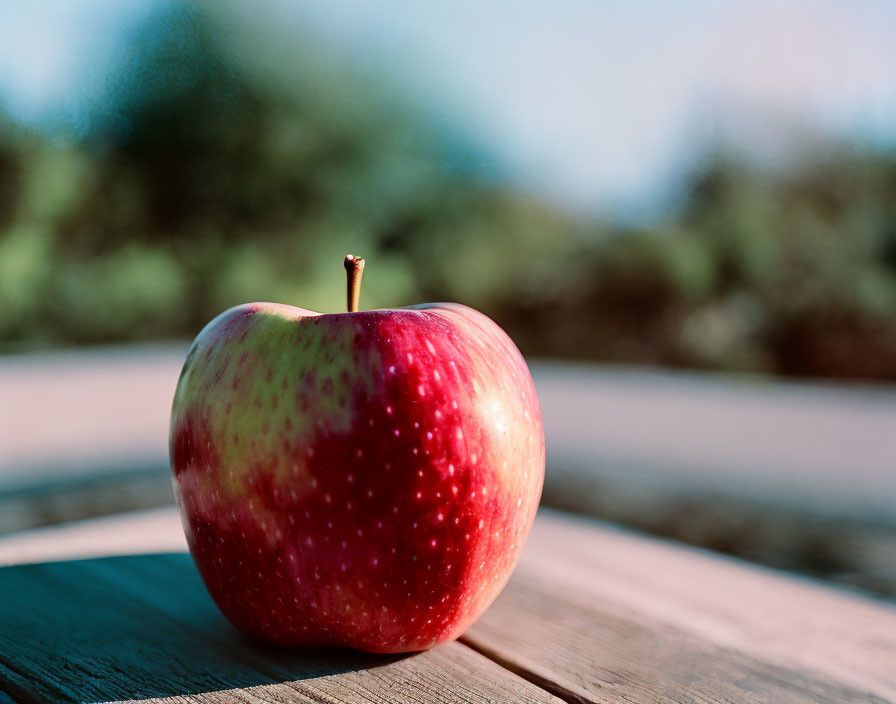 Red apple with green speckles on wooden surface in outdoor setting