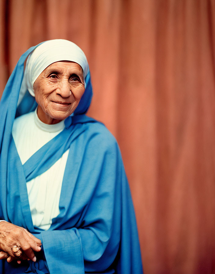 Elderly woman in white headdress and blue robe smiling