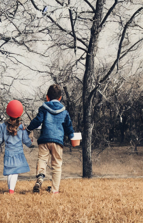 Children with red balloon and bucket in field with bare trees