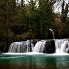 Tranquil waterfall and lake with lush trees under dark sky