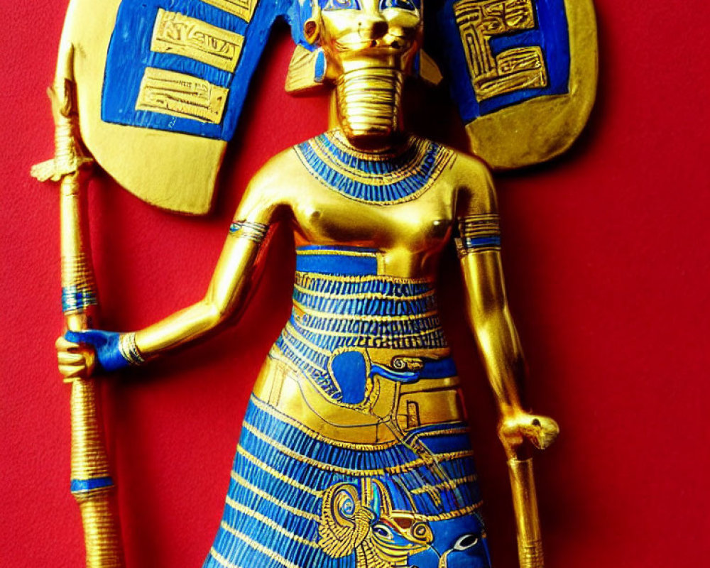 Golden and blue ancient Egyptian deity figurine with staff on red background