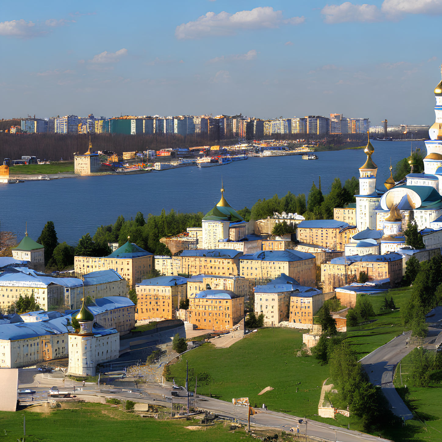 Urban landscape featuring river, residential buildings, golden-domed church, and greenery under blue sky.