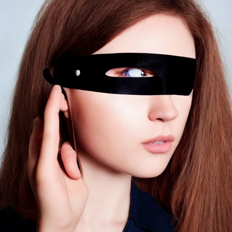 Person with long brown hair wearing black eye mask, touching it.