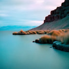 Tranquil lake scene: overcast sky, reeds, distant cliff, serene blue-green tone