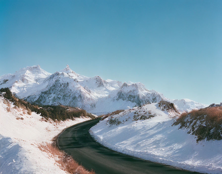 Scenic snow-covered mountains under clear blue sky on winding road